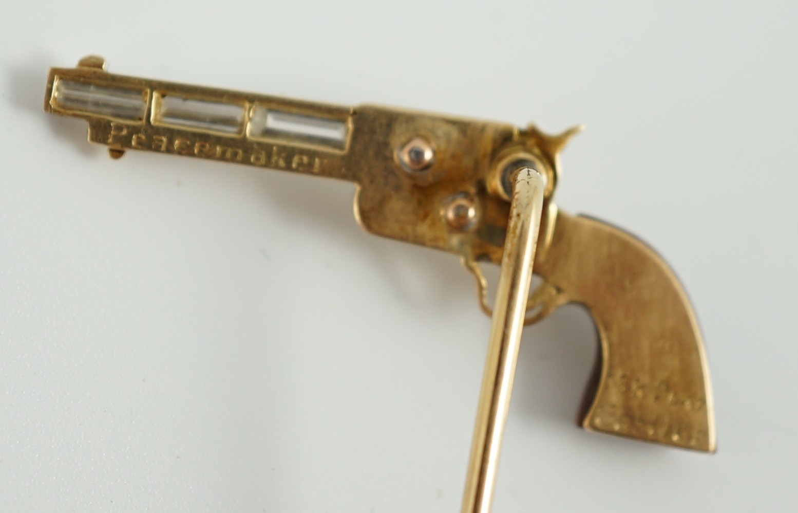 A Cartier 18k gold, platinum and six stone baguette cut diamond set novelty stick pin, modelled and a pistol inscribed 'Peacemaker'